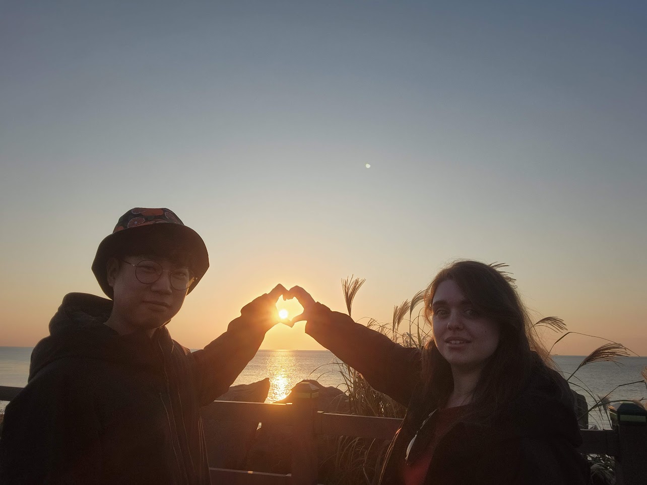 The couple making a heart with their hands at sunset in Jeju